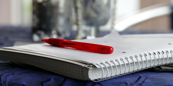 Schreibblock mit Stift Schreibblock mit rotem Stift liegt aufgeschlagen auf einem Tisch