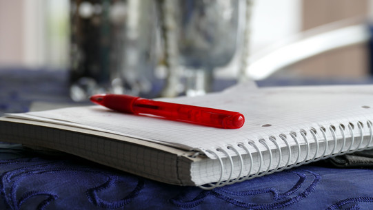 Schreibblock mit Stift Schreibblock mit rotem Stift liegt aufgeschlagen auf einem Tisch