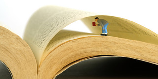 A miniature man searching a data on an opened book