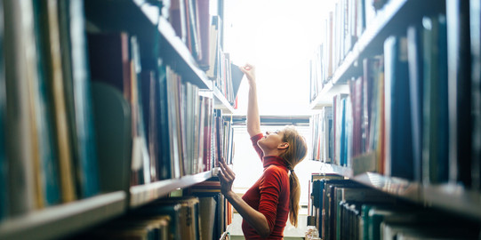 Young woman at the bookshelf Young woman looking for books on shelf and pulls one out