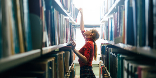 Junge Frau sucht Bücher am Regal und zieht eins heraus