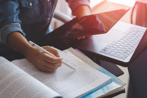 Young woman with a pen in her hand works with a tablet, a laptop and books 