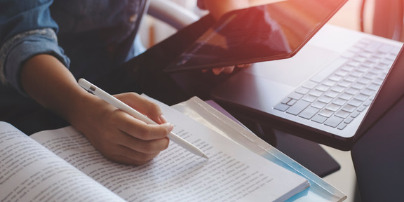 Junge Frau mit einem Stift in der Hand arbeitet mit einem Tablet, einem Laptop und Büchern 