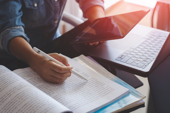Frau mit Tablet, Laptop, Büchern Junge Frau mit einem Stift in der Hand arbeitet mit einem Tablet, einem Laptop und Büchern