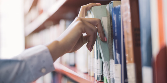 A student pulls out a gray book from a red shelf