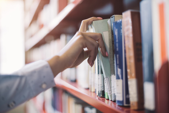 Student pulls book from shelf A student pulls out a gray book from a red shelf