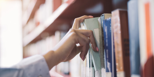 Student pulls book from shelf A student pulls out a gray book from a red shelf