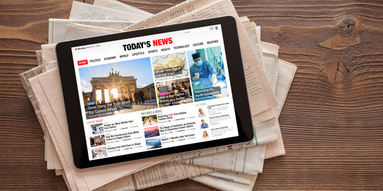 Tablet with news website on stack of newspapers A tablet with a news website lies on a stack of newspapers