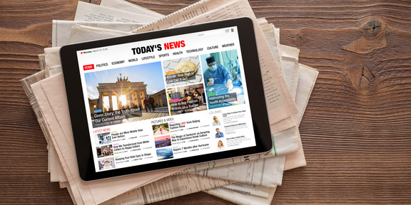 A tablet with a news website lies on a stack of newspapers