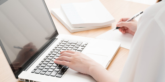 Junge Frau im Profil sitzt an offenem Laptop an einem Tisch, daneben Bücher