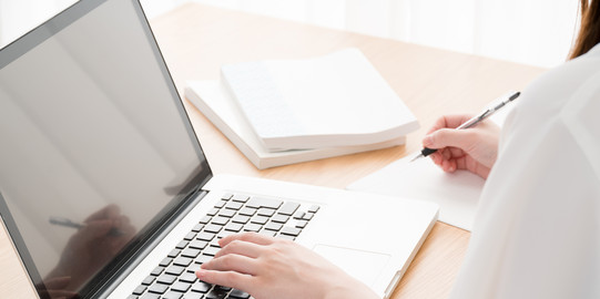 Young woman in profile sitting at open laptop at table, books next to it