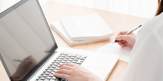 Young woman in profile sitting at open laptop at table, books next to it