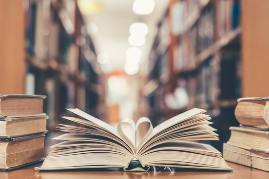 Book with open page of literature in heart shape and stack of textbooks lying on a table