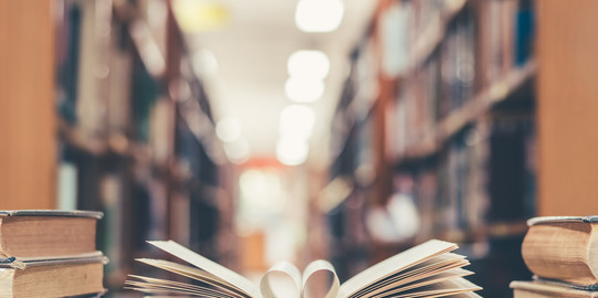 Open book with heart shaped pages in the middle Book with open page of literature in heart shape and stack of textbooks lying on a table