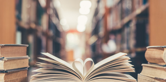 Ein aufgeklapptes Buch liegt mit zu einem Herz geformten Seiten auf dem Tisch neben weiteren Büchern