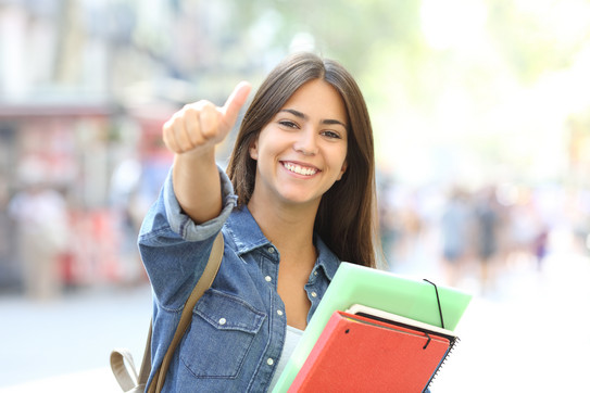 Happy student with booklets A happy student with booklets in her arm gives the thumbs up