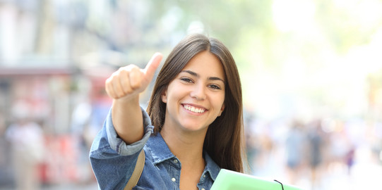 Happy student with booklets A happy student with booklets in her arm gives the thumbs up