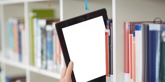 A hand pulls a tablet from a bookshelf in a library