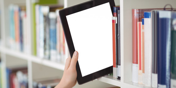 Hand pulls tablet from a bookshelf A hand pulls a tablet from a bookshelf in a library
