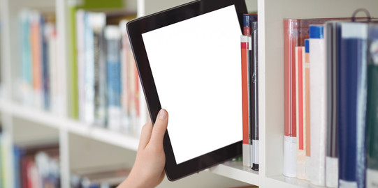 Eine Hand zieht ein Tablet aus einem Bücherregal in einer Bibliothek