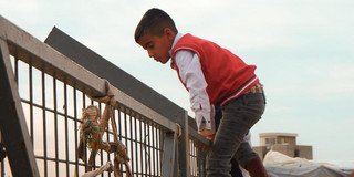 Ein Junge klettert über einen hohen Zaun