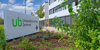 Wegweiser Sebrath-Bibliothek Großes weißes Schild mit Pfeil weist zum Gebäude Sebrathweg 7
