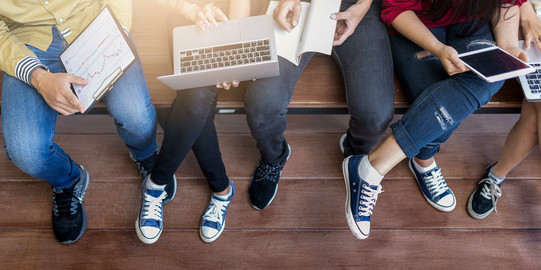 Die Beine von fünf jungen Menschen, die mit Tablet und Laptop lernen