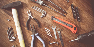 Auf einem Holztisch liegen ein Hammer, verschiedene Zangen, Imbusschlüssel, Schrauben, Schraubenzieher, Dübel etc.