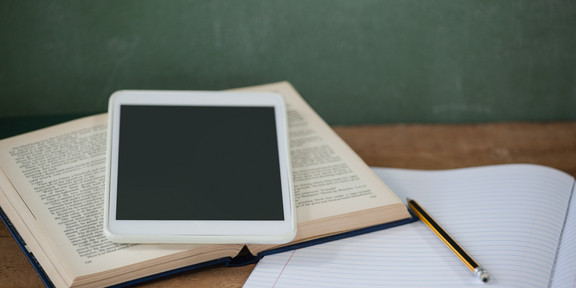 Ein Tablet, ein Buch und ein Heft liegen auf einem Tisch