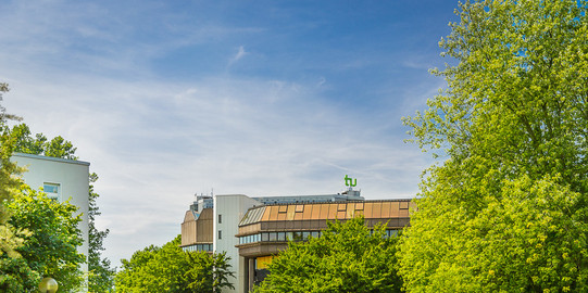 Gebäude der Universitätsbibliothek im Sommer, im Vordergrund grüne Bäume
