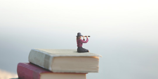 Miniaturfrau schaut mit dem Fernrohr auf einem Bücherstapel in die Unendlichkeit