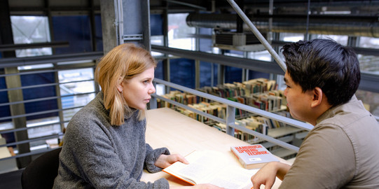 Two students sit working at a table in the library.
