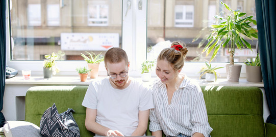 Two students working on a laptop, sitting on a sofa.