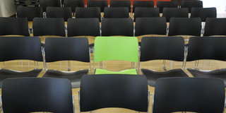 Ein grüner Stuhl inmitten von schwarzen Stühlen