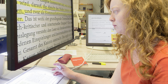 Eine Studentin sitzt an einem Computer und liest einen Text in großer Schrift.