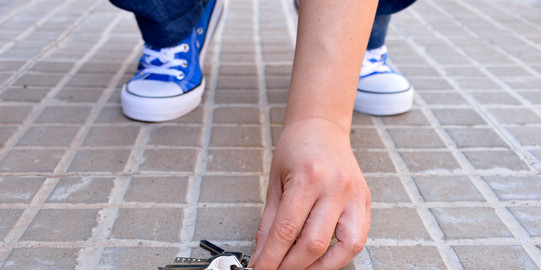 Close-up of hands picking up a bunch of keys from the street.