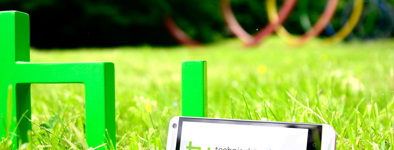 TU app The green logo of TU Dortmund University is standing on a meadow. A smartphone is leaning against it.