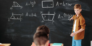 Ein Junge steht an der Tafel und erklärt Mathe