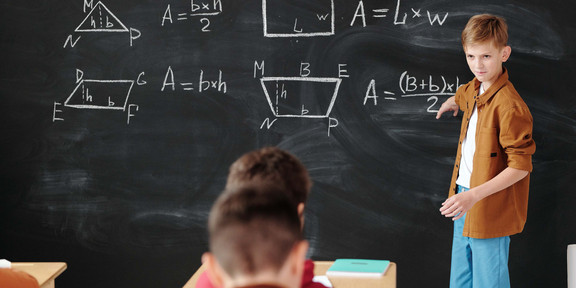 A boy stands at the blackboard and explains math