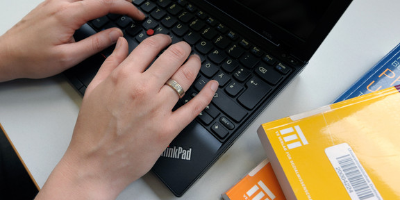 A student types on a laptop and yellow books lay next to it.