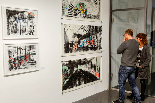 Exhibition Two persons are looking at pictures at a wall.