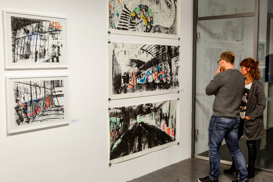 Zwei Menschen betrachten Bilder an der Wand in einer Ausstellung.
